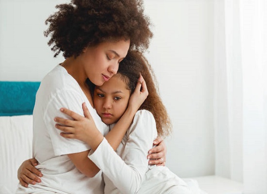 Mother comforting her daughter, sitting in the bedroom, hugging